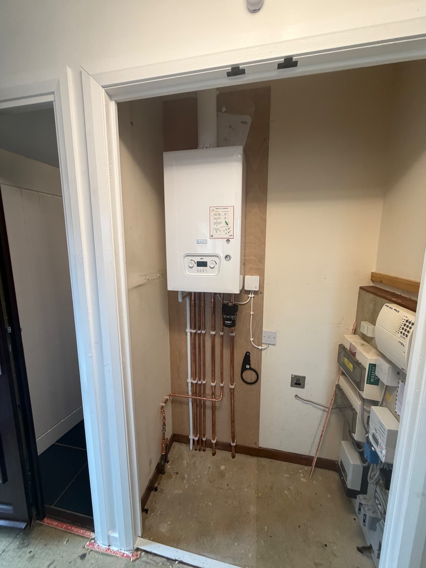 Wall-mounted Baxi boiler fitted in a hallway cupboard beside the electrical meters